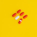 Red capsules and a white tablet arranged on a bright yellow surface, symbolizing healthcare.