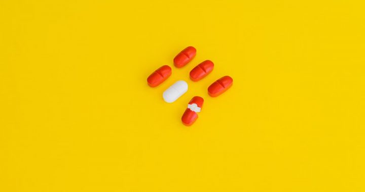 Red capsules and a white tablet arranged on a bright yellow surface, symbolizing healthcare.