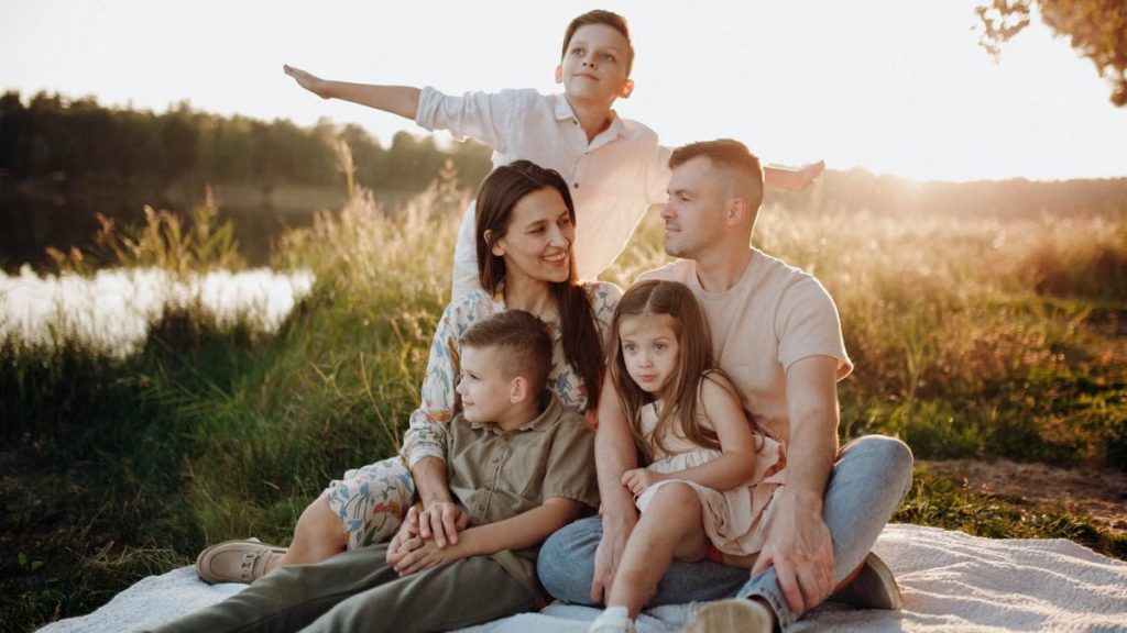 A family of five enjoying a serene picnic in a sunlit meadow during sunset.