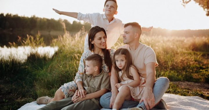 A family of five enjoying a serene picnic in a sunlit meadow during sunset.