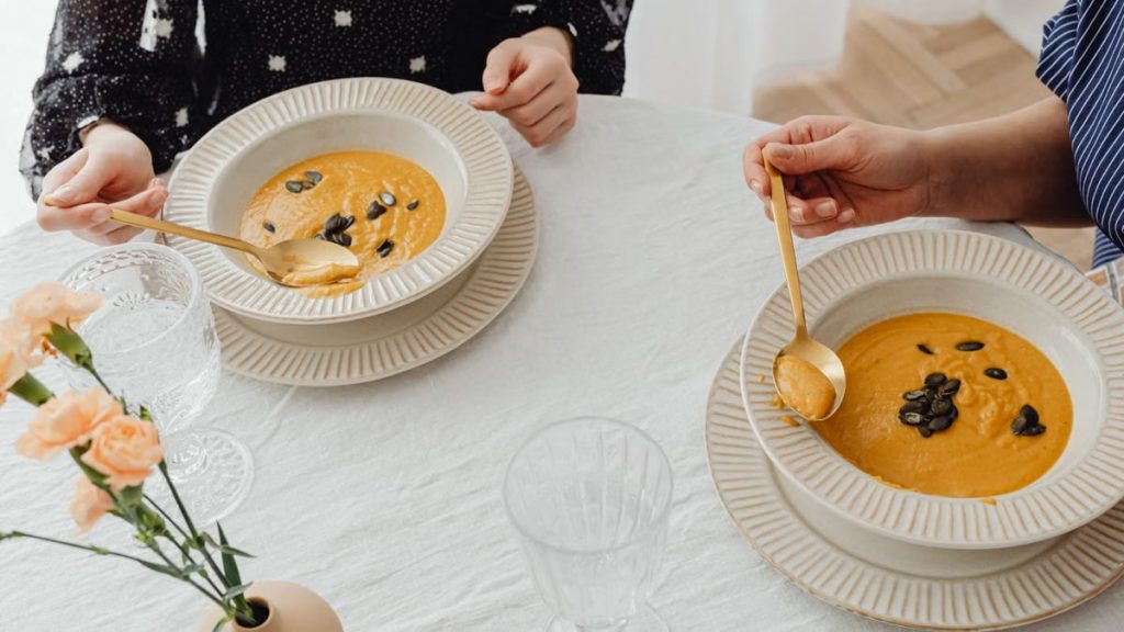 A top view of two people enjoying creamy pumpkin soup with elegant table setting.