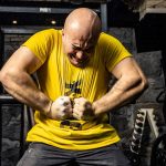 Bald muscular man in yellow t-shirt showcasing strength in a gym, highlighting intense dedication.