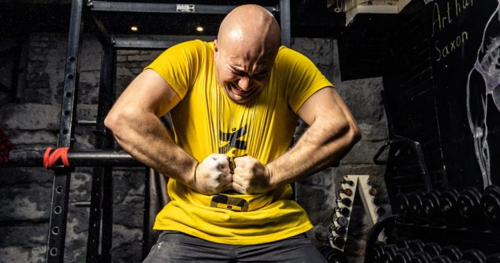 Bald muscular man in yellow t-shirt showcasing strength in a gym, highlighting intense dedication.